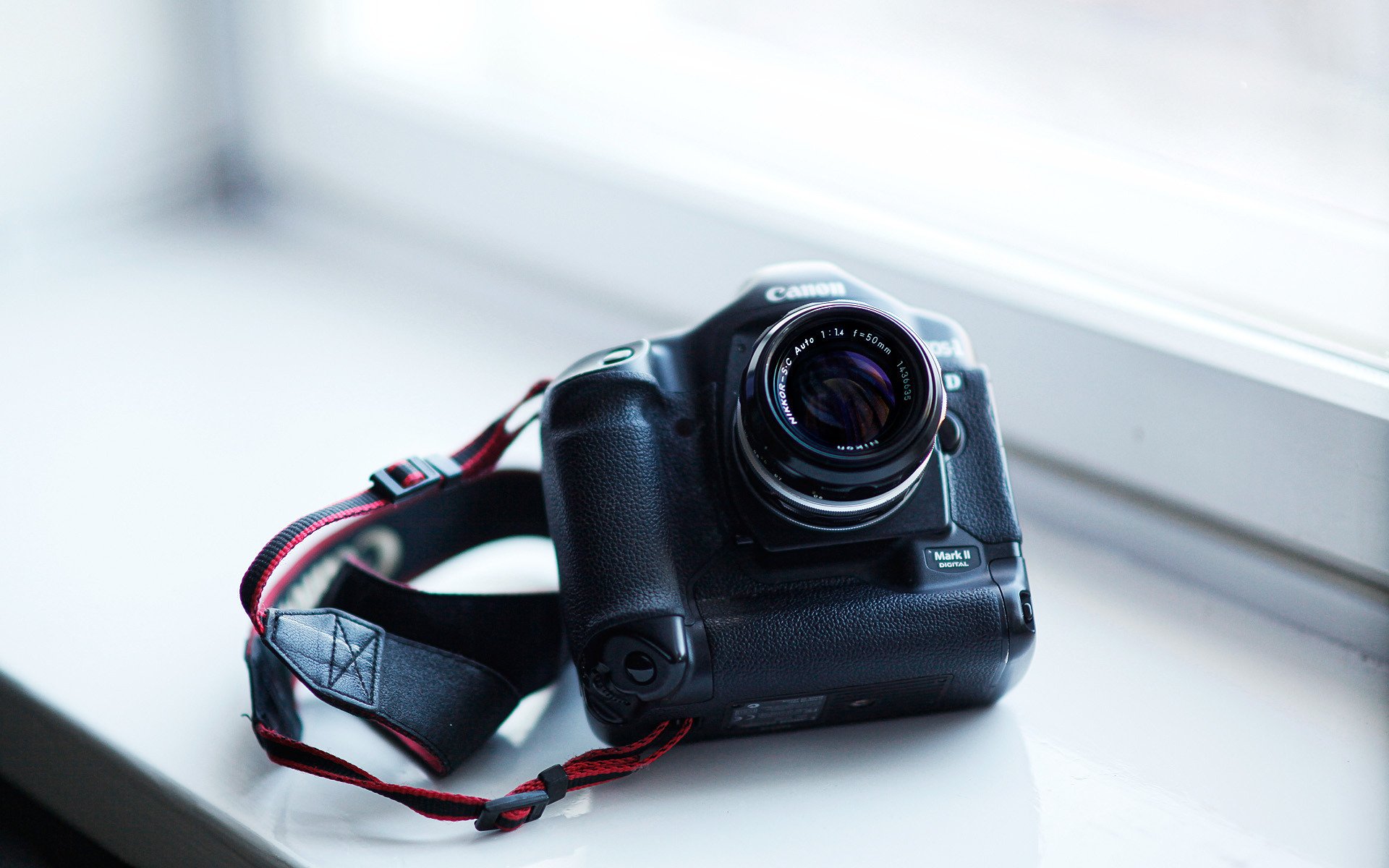 Black camera with lens and strap resting on a windowsill, minimalist HD PC desktop wallpaper and background highlighting a man-made camera.