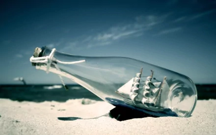 HD desktop wallpaper featuring a man-made ship in a bottle resting on sand with the ocean and sky in the background.