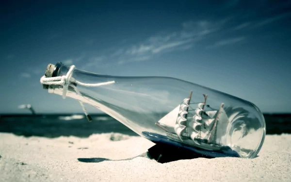 HD desktop wallpaper featuring a man-made ship in a bottle resting on sand with the ocean and sky in the background.