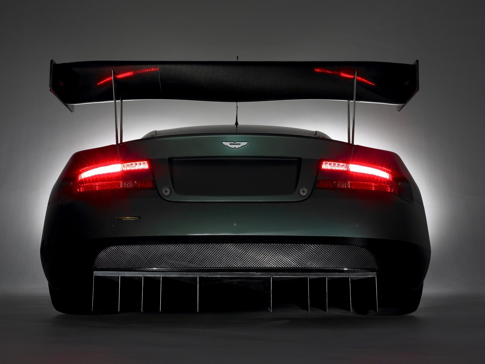Rear view of an Aston Martin DBR9 race car with glowing taillights and aerodynamic wing, presented as an HD PC desktop wallpaper/background.
