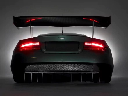 Rear view of an Aston Martin DBR9 race car with glowing taillights and aerodynamic wing, presented as an HD PC desktop wallpaper/background.
