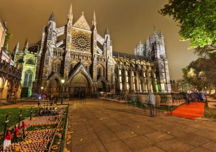 Illuminated Westminster Abbey Gothic façade at night, churchyard and lit pathways — religious 2K Quad HD PC desktop wallpaper background.