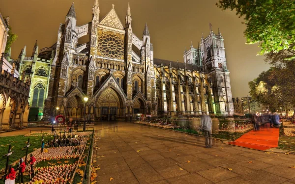 Illuminated Westminster Abbey Gothic façade at night, churchyard and lit pathways — religious 2K Quad HD PC desktop wallpaper background.