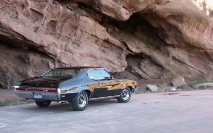 Classic Chevrolet muscle car (rear three-quarter view) parked beside rugged sandstone cliffs, glossy paint reflecting the rock — 4K Ultra HD PC desktop wallpaper and background.