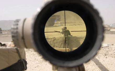 HD PC desktop wallpaper showing a military sniper aiming through a rifle scope at a soldier in a desert environment.