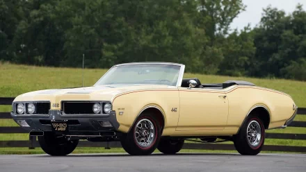 HD desktop wallpaper featuring a classic yellow Oldsmobile 442 convertible parked on a road with greenery in the background.