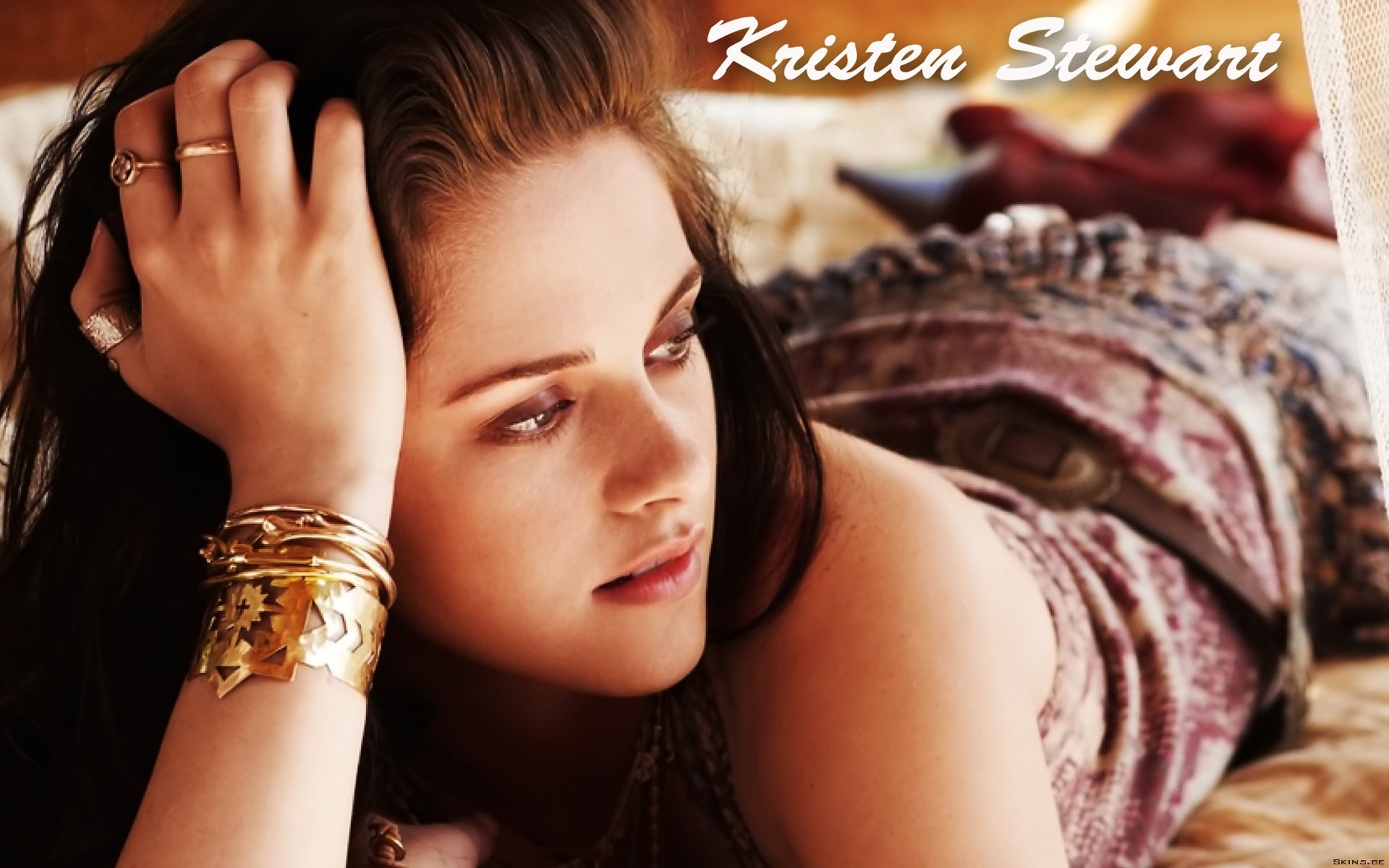 A high-definition desktop wallpaper featuring Kristen Stewart, depicted in a relaxed pose with styled hair and elegant jewelry, capturing her contemplative expression.