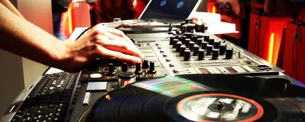 A DJ's hand adjusts the controls of a turntable, capturing the vibrant energy of music in action. This HD desktop wallpaper immerses you in the world of live DJ performances.