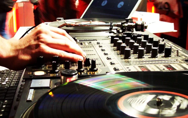 A DJ's hand adjusts the controls of a turntable, capturing the vibrant energy of music in action. This HD desktop wallpaper immerses you in the world of live DJ performances.