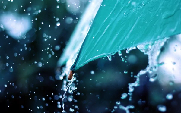 A close-up of a turquoise umbrella catching raindrops, with water splashing around it. This HD photography captures the beauty of rain, making it a stunning desktop wallpaper.