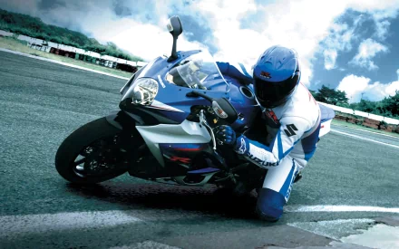 A dynamic HD wallpaper featuring a motorcycle leaning into a curve, with a rider in protective gear, showcasing speed and agility on a racetrack against a dramatic sky.