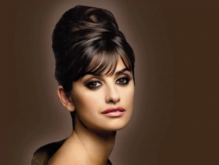 A striking HD wallpaper featuring Penelope Cruz, showcasing her elegant hairstyle and captivating makeup against a warm brown background.