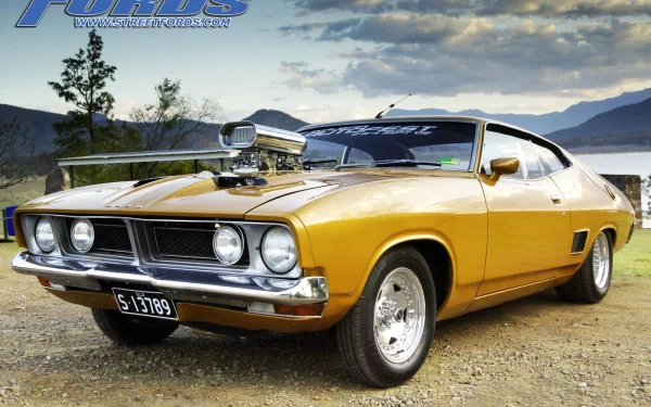 HD desktop wallpaper featuring a Ford XB Falcon vehicle in a scenic outdoor setting, with mountains and trees in the background.