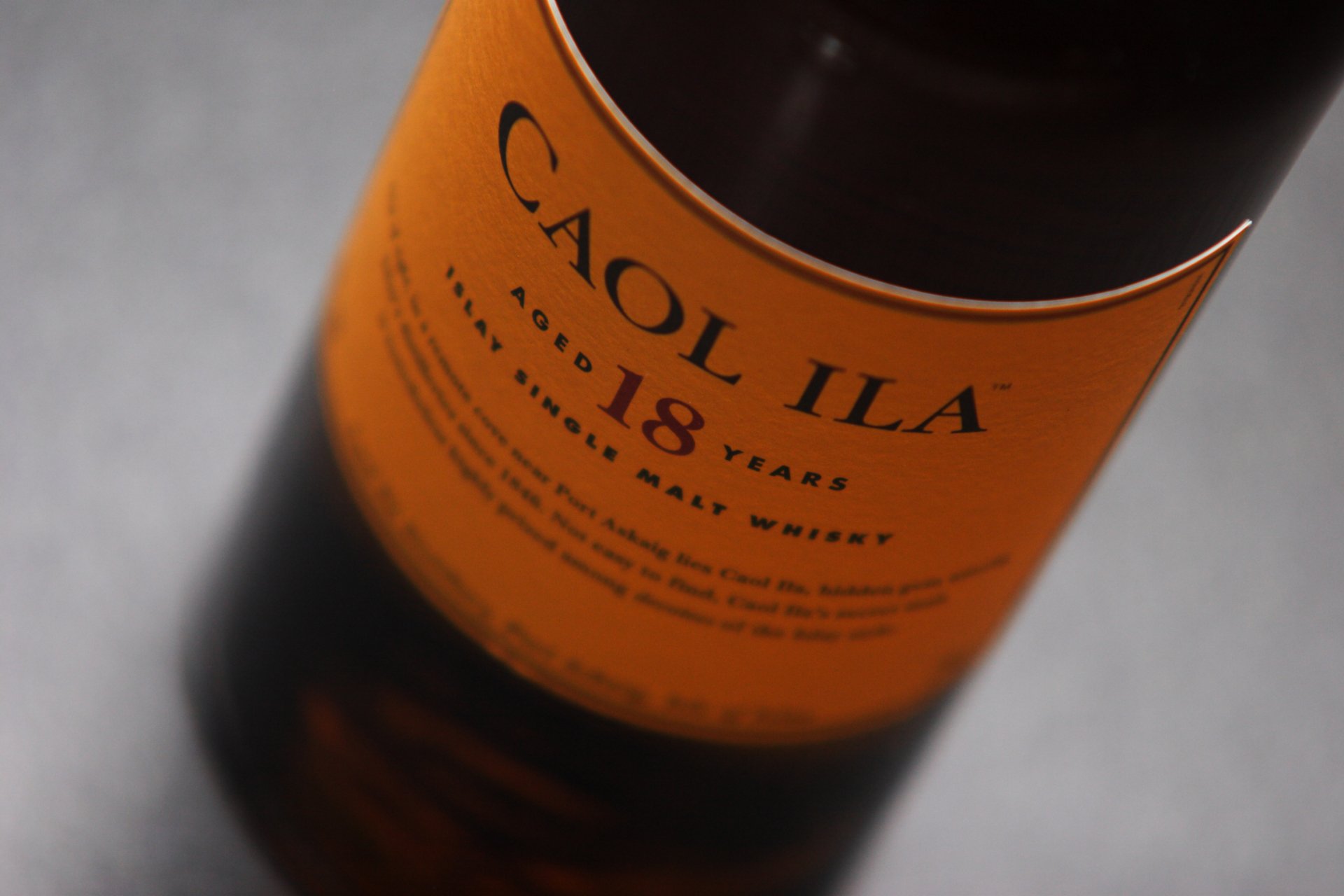 A close-up of a Caol Ila 18 Years old Scotch whisky bottle, showcasing its distinct orange label, set against a neutral background for a sophisticated HD desktop wallpaper.