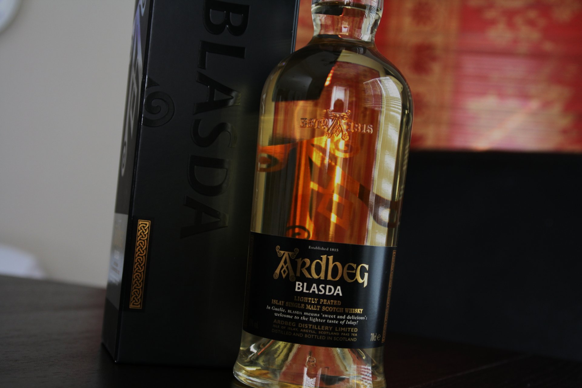 A close-up of an Ardbeg Blasda bottle, showcasing its rich golden whisky, with the elegant box in the background. This 4K Ultra HD wallpaper captures the essence of fine Scotch malt.