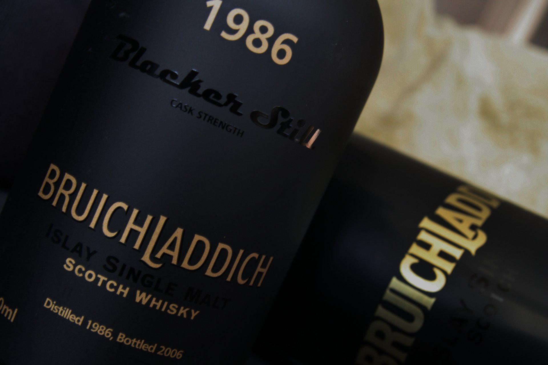 A close-up of Bruichladdich 1986 Scotch whisky bottles, highlighting their elegant black labels and gold lettering, set against a blurred background. 4K Ultra HD wallpaper.