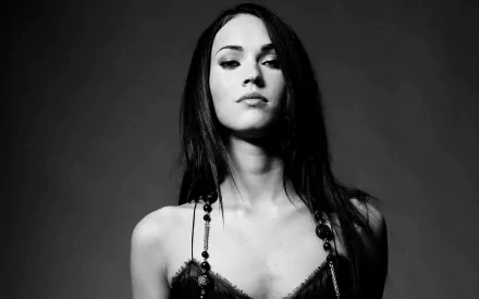 Black and white HD wallpaper featuring Megan Fox, with a confident expression and elegant necklace, against a dark background.