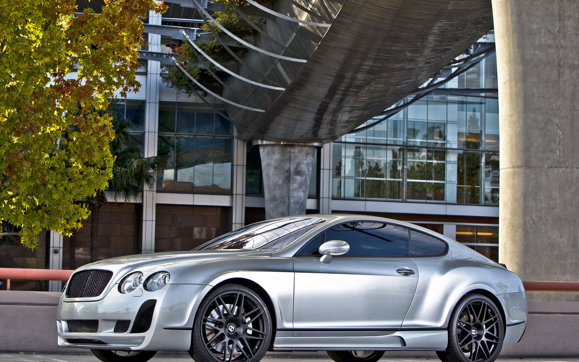 Silver Bentley coupe parked beneath a modern architectural overhang, photographed in HD — PC desktop wallpaper and background highlighting sleek lines and alloy wheels.