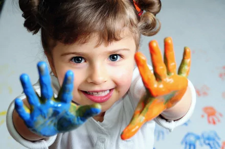 A cute child joyfully displays her paint-covered hands, showcasing vibrant colors. This HD image serves as a delightful desktop wallpaper, capturing the essence of creativity and fun.