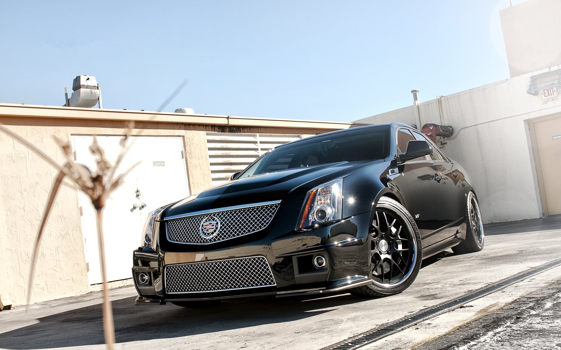 HD PC desktop wallpaper featuring a sleek black Cadillac parked in an urban setting with sunlight highlighting its polished exterior and detailed grille.