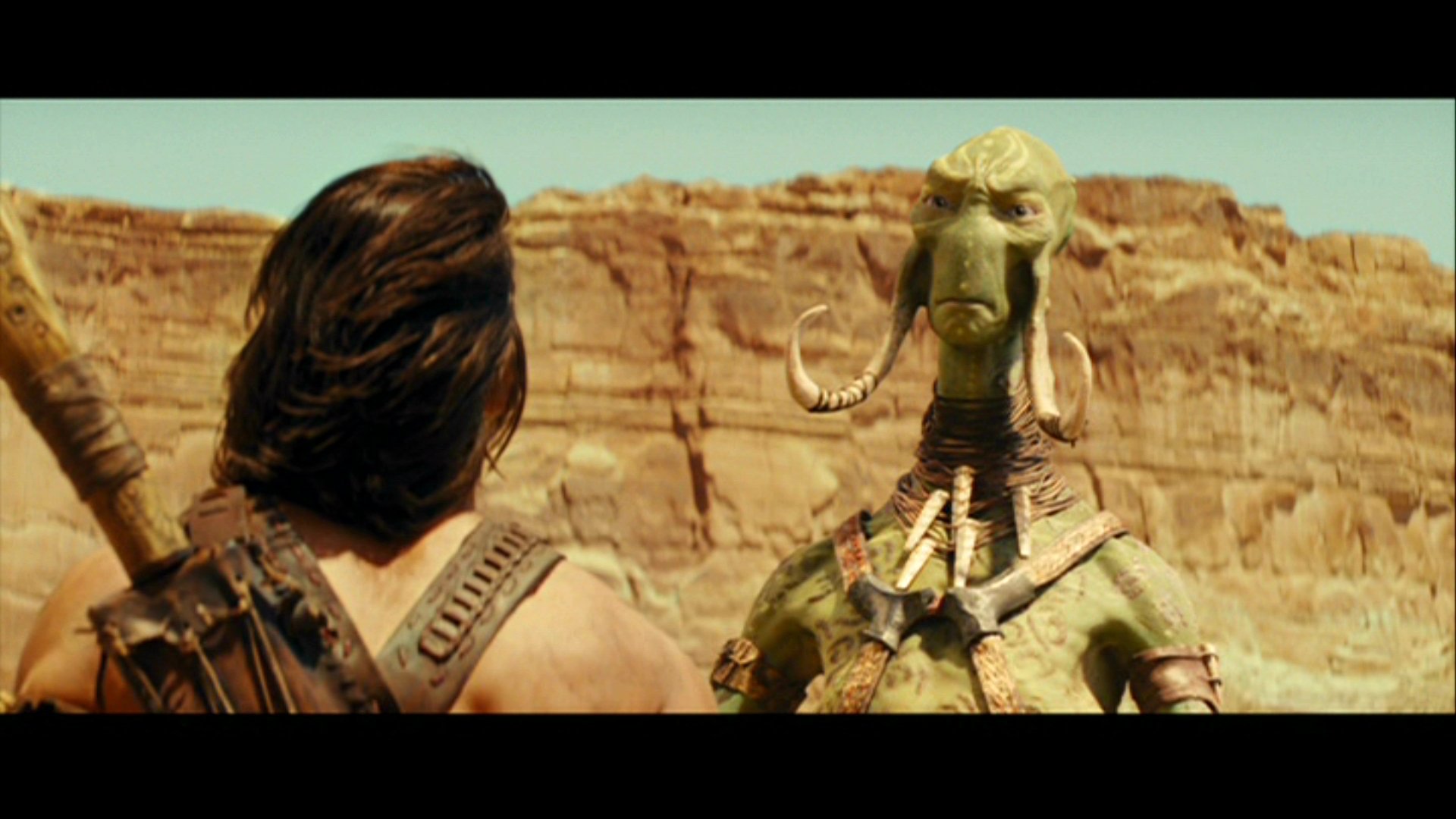 HD PC desktop wallpaper from the movie John Carter: back-view of John Carter facing a tall green alien warrior against a sunlit canyon background.