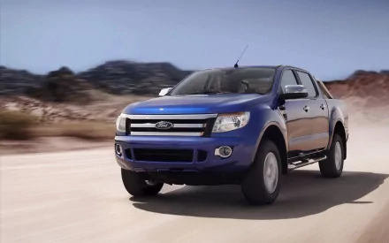 HD PC desktop wallpaper featuring a blue Ford Ranger driving on a dusty road with blurred desert terrain in the background.