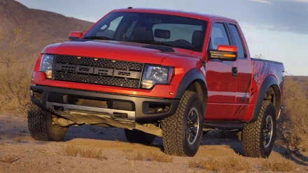 Red Ford Raptor vehicle parked on desert sand, rugged off-road stance — HD PC desktop wallpaper background showing a front three-quarter view.