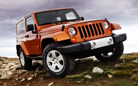 An orange Jeep parked on rocky terrain, showcasing its rugged design against a dramatic sky, making it an engaging HD desktop wallpaper and background.