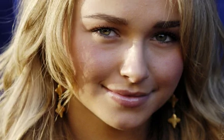 HD desktop wallpaper featuring close-up of a smiling person tagged as celebrity Hayden Panettiere, with wavy blonde hair and star-shaped earrings.