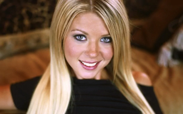 A close-up portrait of Tara Reid, showcasing her long blonde hair and radiant smile, set against a soft blurred background, designed as an HD desktop wallpaper.