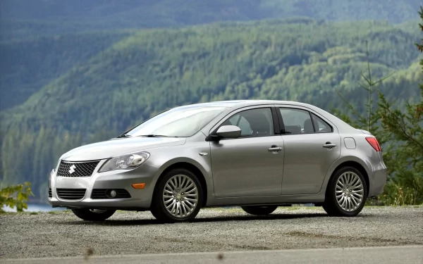 HD PC desktop wallpaper of a silver Suzuki sedan vehicle parked on a roadside with green, misty mountains in the background.