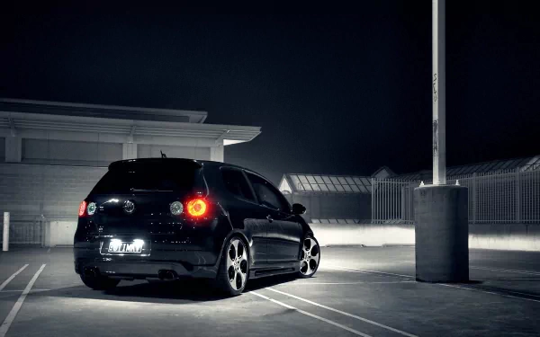 A sleek black Volkswagen vehicle parked in a dimly lit area, showcasing its stylish design and modern features against a nighttime backdrop. HD desktop wallpaper.