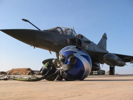 HD wallpaper and background image of a military jet fighter grounded, with a pilot’s helmet placed on the tarmac in the foreground under a clear blue sky.
