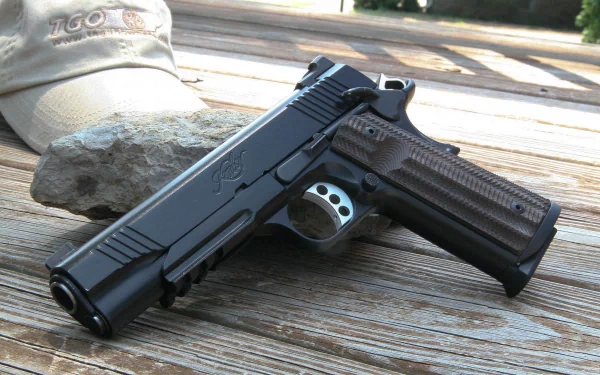 A close-up view of a Kimber pistol resting on a wooden surface, accompanied by a rock and a cap in the background. This high-definition image serves as a striking desktop wallpaper.