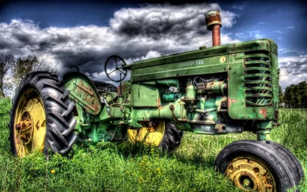 A vibrant HD wallpaper featuring a classic John Deere tractor resting in lush green grass under a dramatic sky, showcasing its vintage design and rich colors.