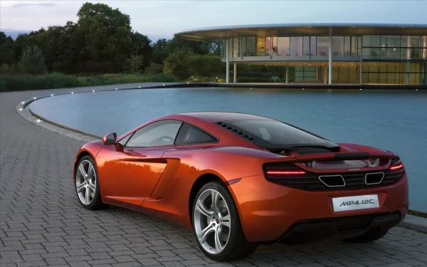 A stunning HD desktop wallpaper featuring an orange McLaren MP4-12C, parked by a pool with a modern building and greenery in the background.