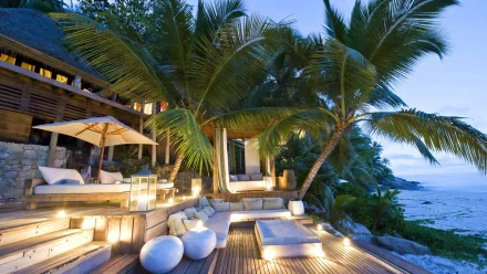 A serene tropical resort in the Seychelles, featuring lush palm trees and a cozy outdoor seating area, illuminated by soft lights against a tranquil ocean backdrop.
