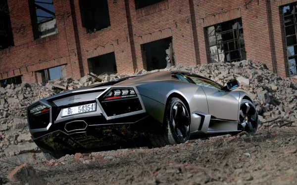 HD desktop wallpaper showing a sleek silver Lamborghini Reventon parked on rough terrain in front of a weathered brick building with broken windows.