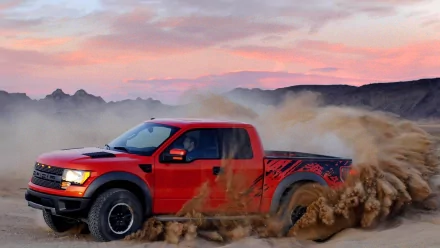 HD PC desktop wallpaper of a red Ford Raptor driving through a dusty desert landscape at sunset.