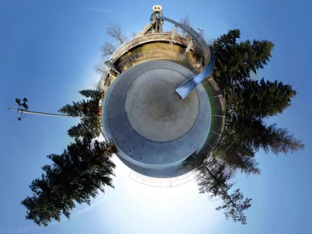 A distorted, panoramic view of a park featuring a circular skating area surrounded by trees, presented as an HD desktop wallpaper and background with a creative photographic manipulation style.