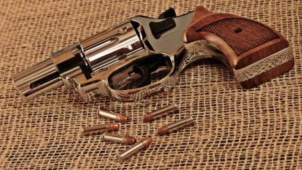 HD desktop wallpaper featuring a detailed revolver with a wooden grip and six bullets, showcased on a textured burlap background.