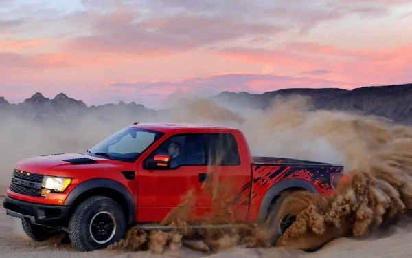 HD PC desktop wallpaper of a red Ford Raptor driving through a dusty desert landscape at sunset.