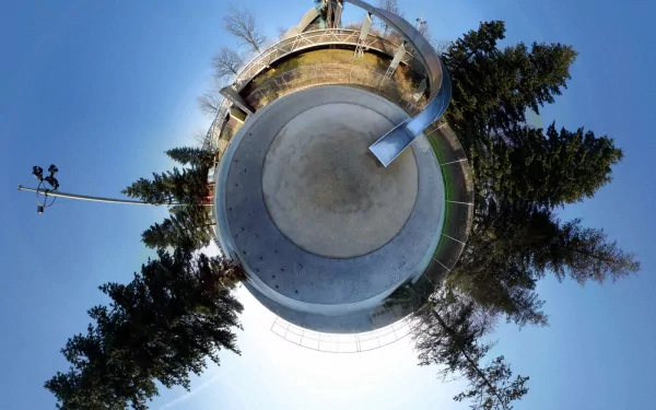A distorted, panoramic view of a park featuring a circular skating area surrounded by trees, presented as an HD desktop wallpaper and background with a creative photographic manipulation style.