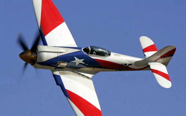 HD PC desktop wallpaper background of a red-white-blue military aircraft with spinning propeller soaring across a clear blue sky.