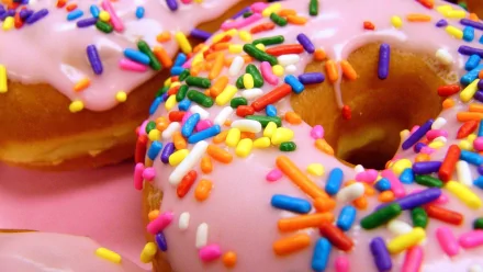 Close-up of colorful doughnuts with pink icing and vibrant sprinkles, set against a bright background, making an appetizing HD wallpaper for any desktop.