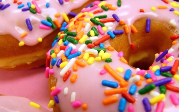 Close-up of colorful doughnuts with pink icing and vibrant sprinkles, set against a bright background, making an appetizing HD wallpaper for any desktop.