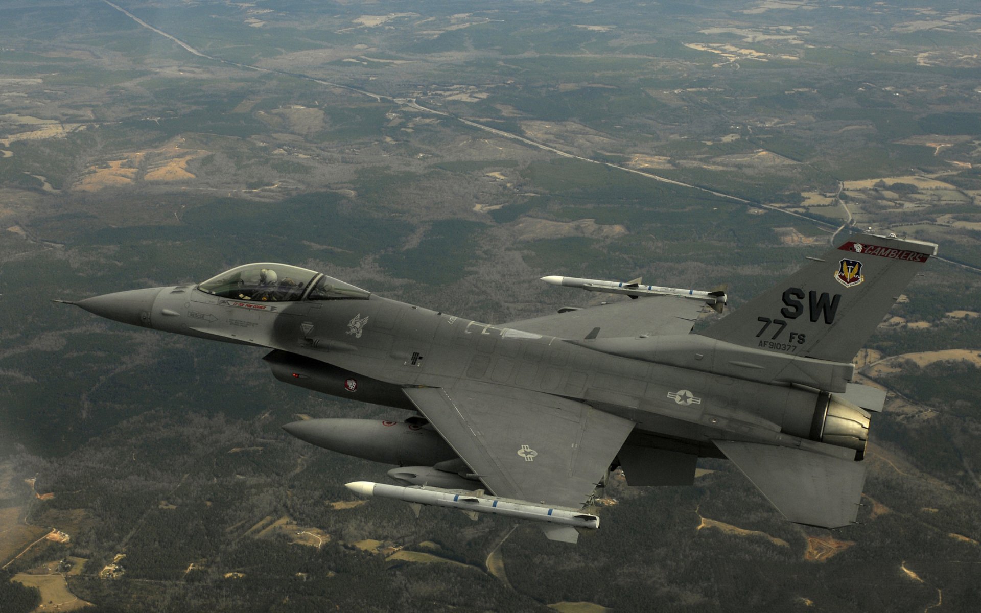 High-definition desktop wallpaper featuring a General Dynamics F-16 Fighting Falcon military jet soaring above a landscape.