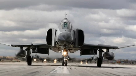 A McDonnell Douglas F-4 Phantom II military jet approaches the runway, surrounded by dramatic clouds, showcasing its sleek design and power in this HD desktop wallpaper.