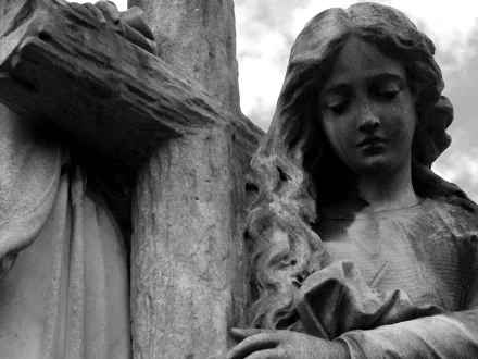 A close-up of a man-made statue featuring a cross and a contemplative figure, set against a cloudy sky, creating a serene and reflective atmosphere.