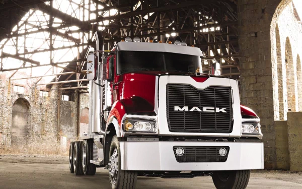 Front view of a red Mack Trucks big rig semi parked in a weathered industrial warehouse — HD PC desktop wallpaper/background featuring the heavy-duty vehicle.